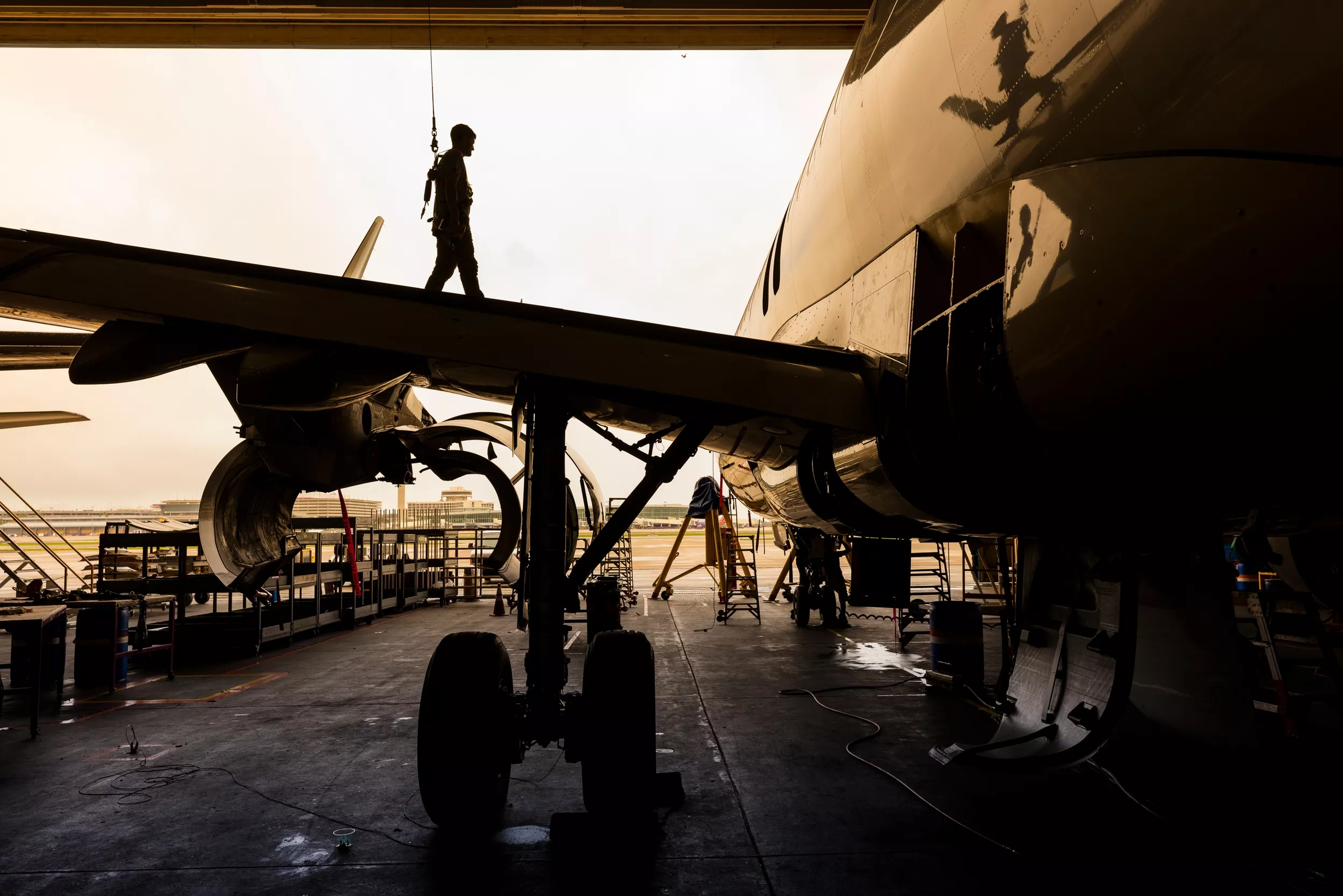 Sillhouette of person walking across airplane wing while docked in hangar.