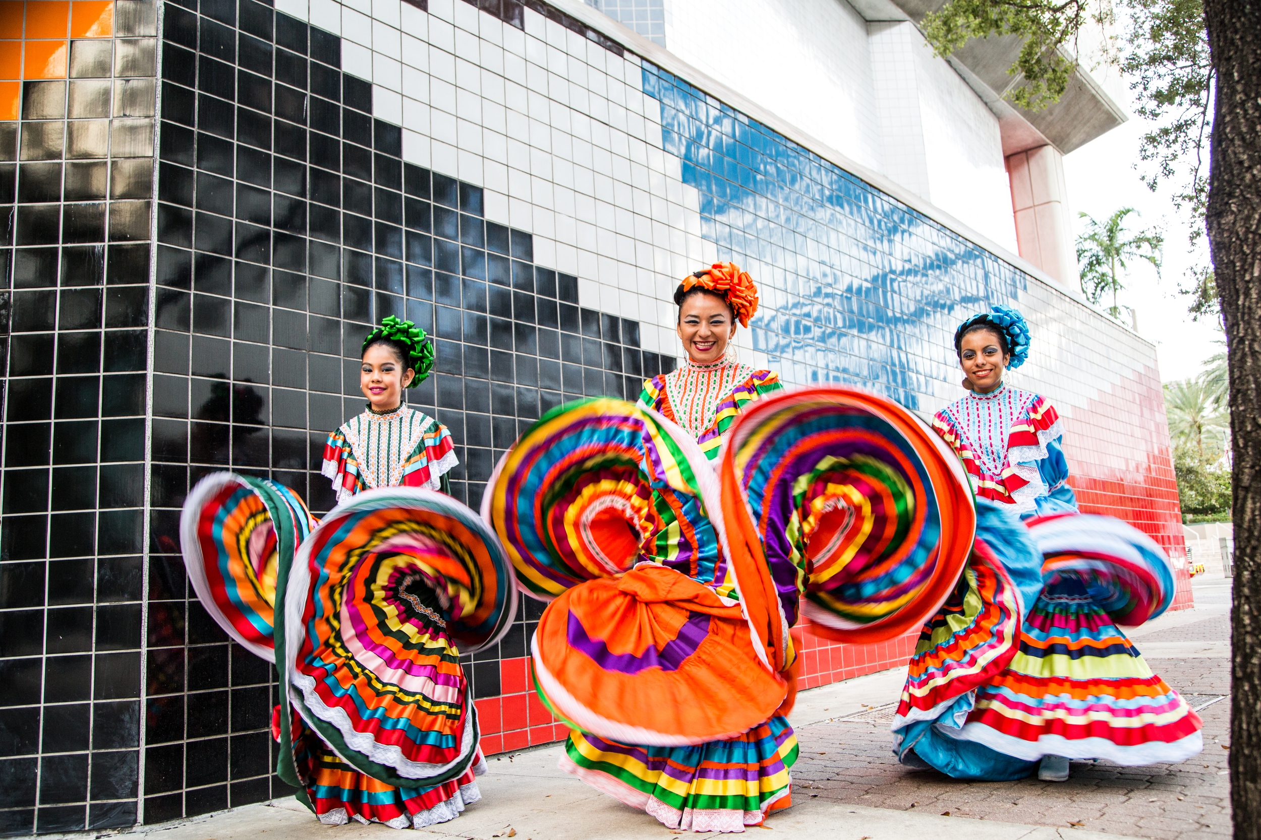 Three female folklorico azteca dancers, smiling and showing their colorful dresses.